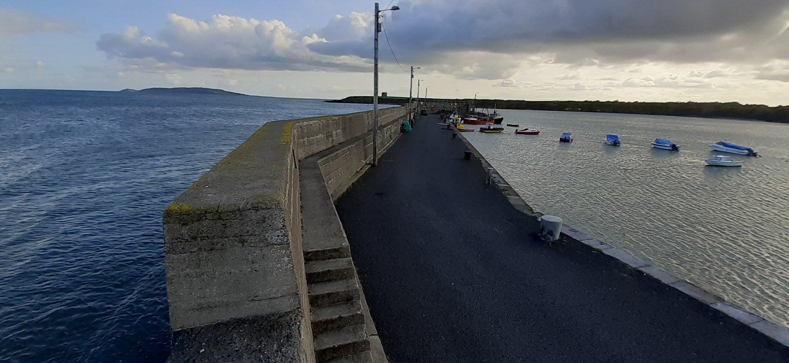 The stone pier at Loughshinny harbour, County Dublin, on a cloudy morning, with small boats moored on calm water